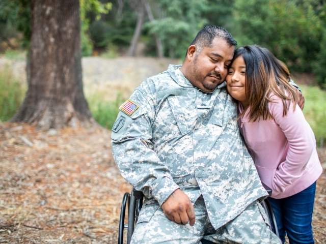 Man in camouflage in wheelchair, veteran, with his arm around woman, both smiling