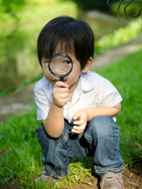 Young boy outdoors looking at the camera through a magnifying glass