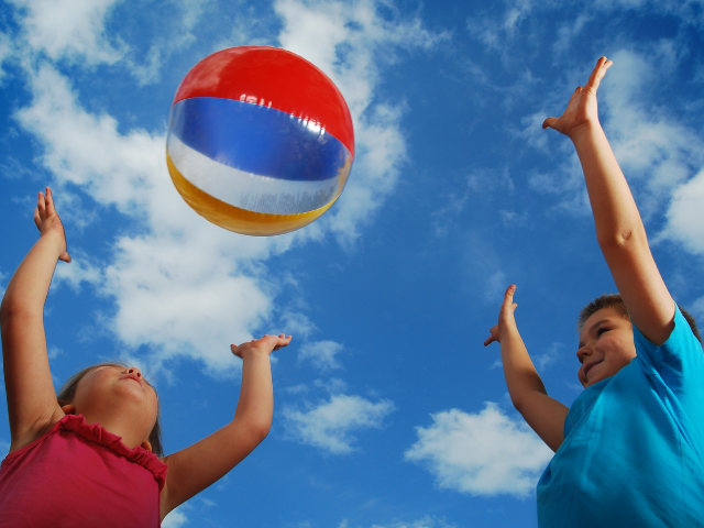 Two children tossing a beachball towards the sky