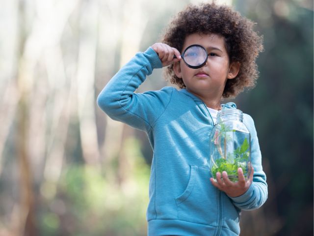 a child holds a jar of water looking through a magnifying glass