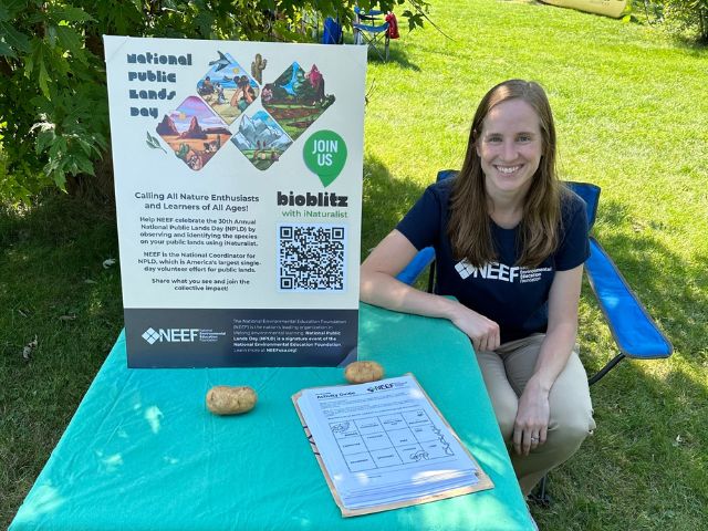 NEEF staff Megan Willig sits a table with a BioBlitz info sign at an NPLD Event in Milwaukee, WI