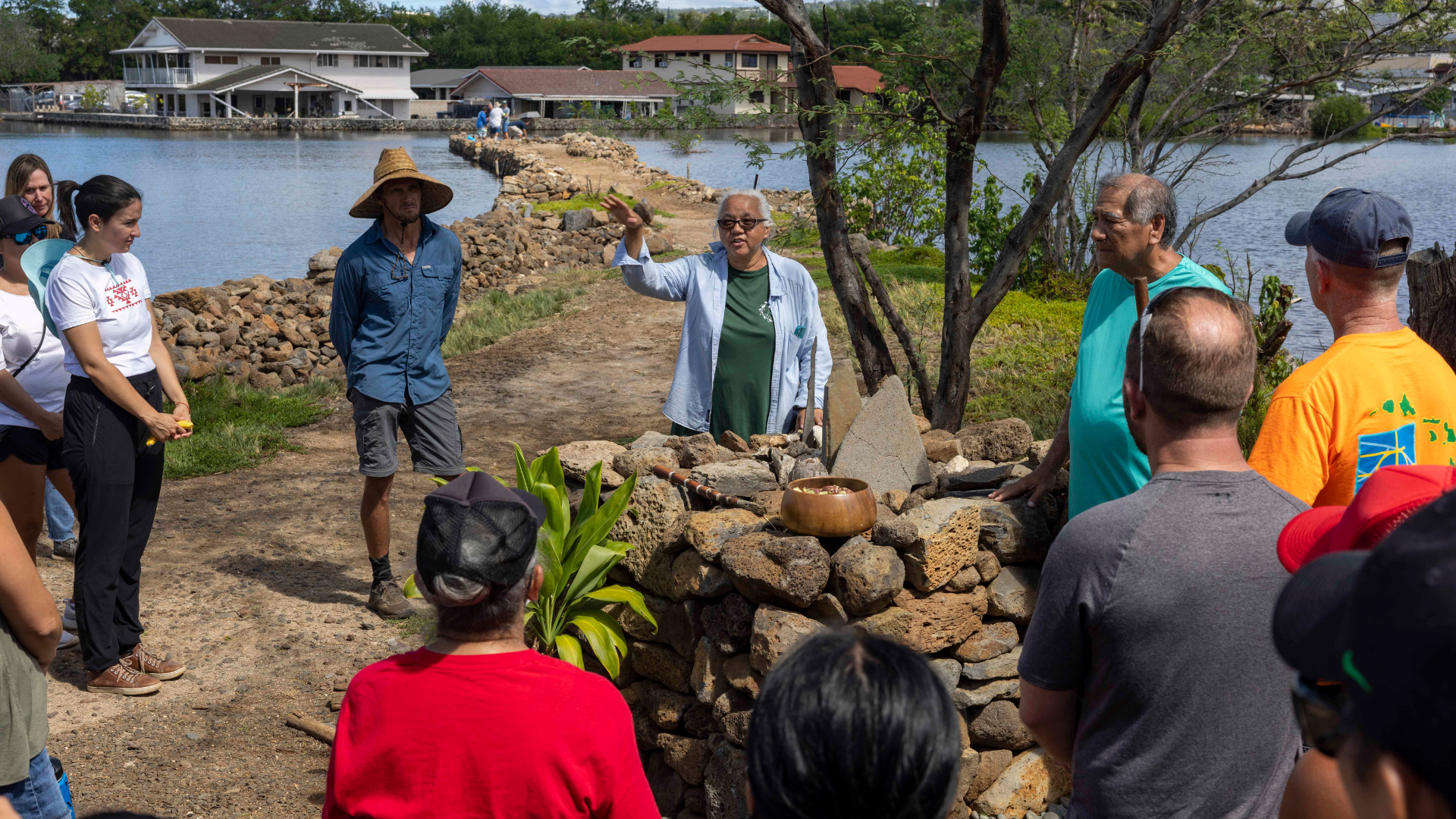 A group gathers around a stone altar as an elder from the Native Hawaiian community explains the significance of the sacrificial offerings placed there