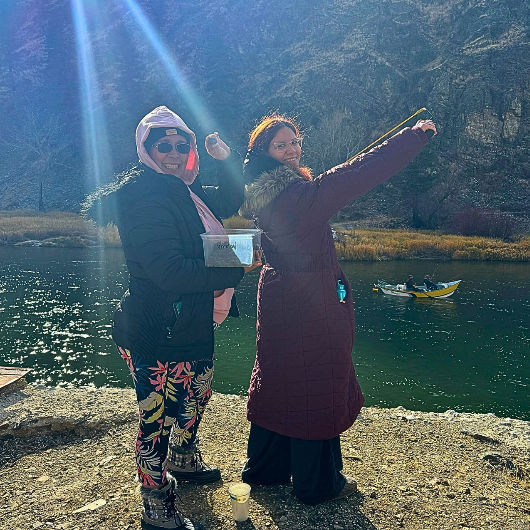 Two people standing by water with seedballs and a sling shot