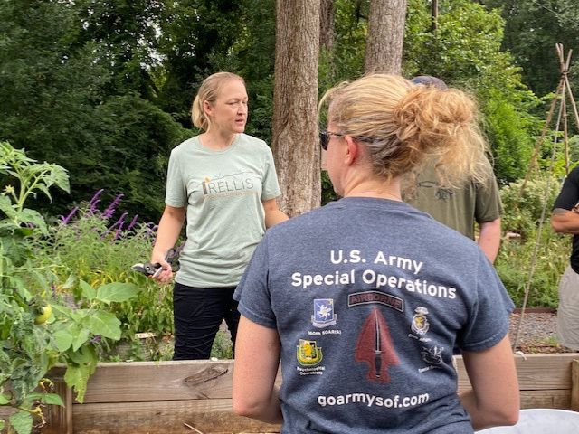two women stand around a raised bed garden, one wears a US Army Special Operations t-shirt