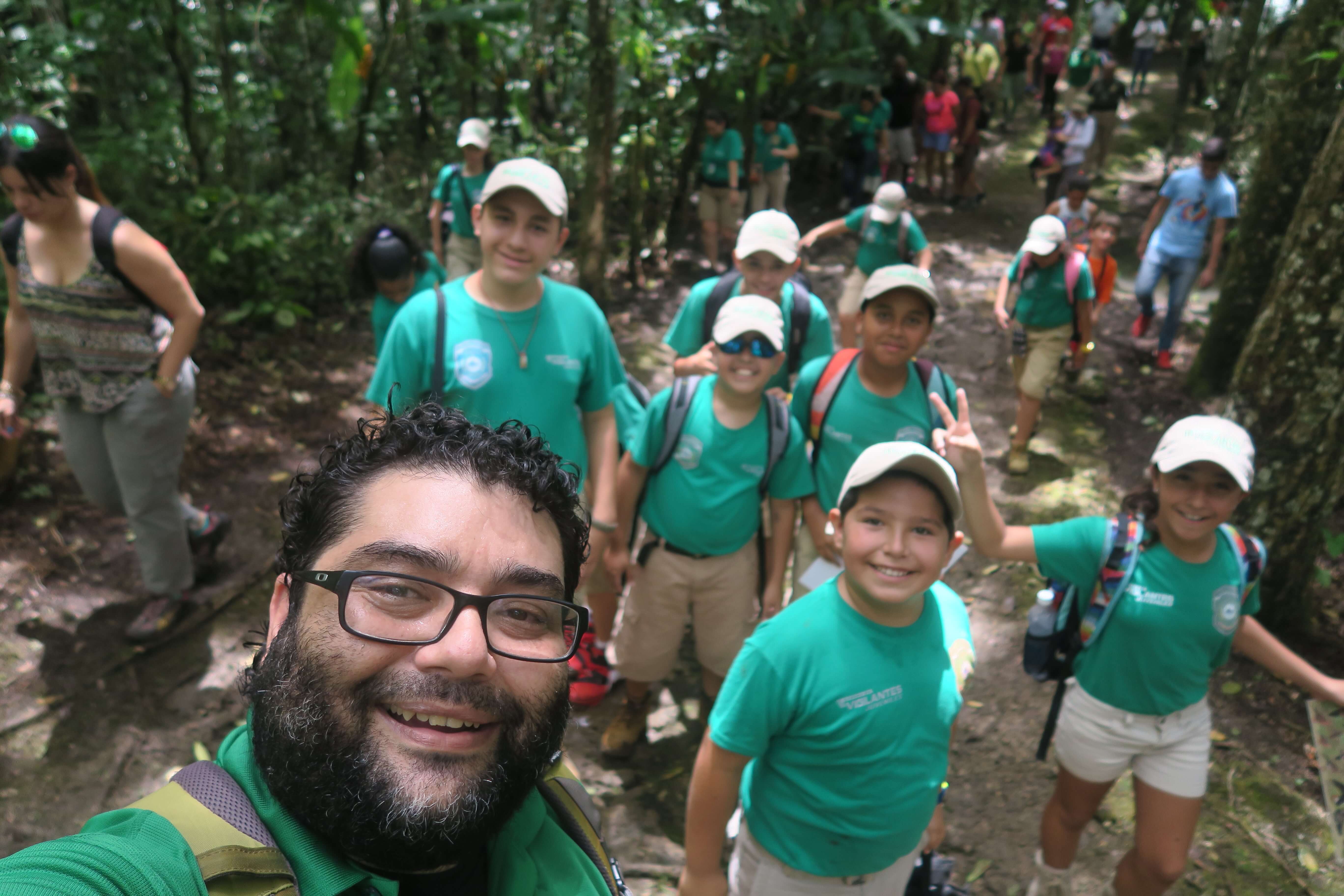 selfie of male volunteer with a group of kids wearing green tshirts on trail in forest