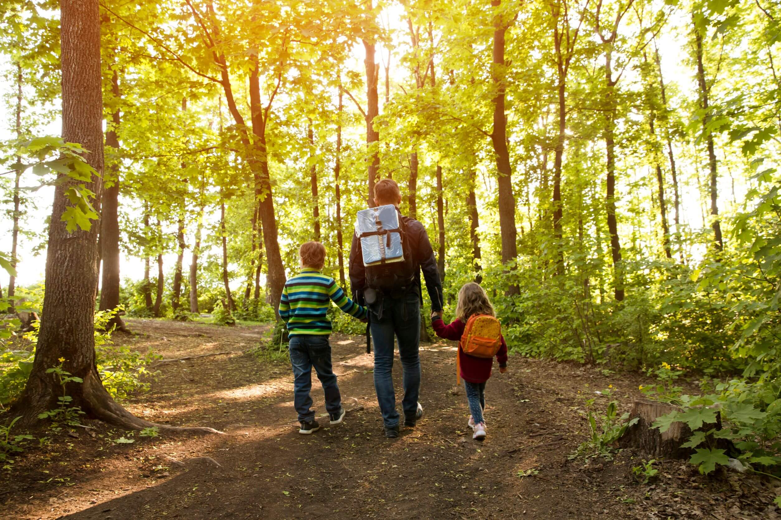 father hiking with two kids in forest holding hands wearing backpacks