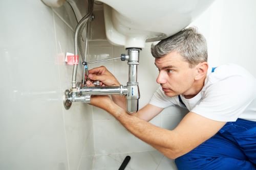 man fixing under a sink to stop leaky faucet from wasting water