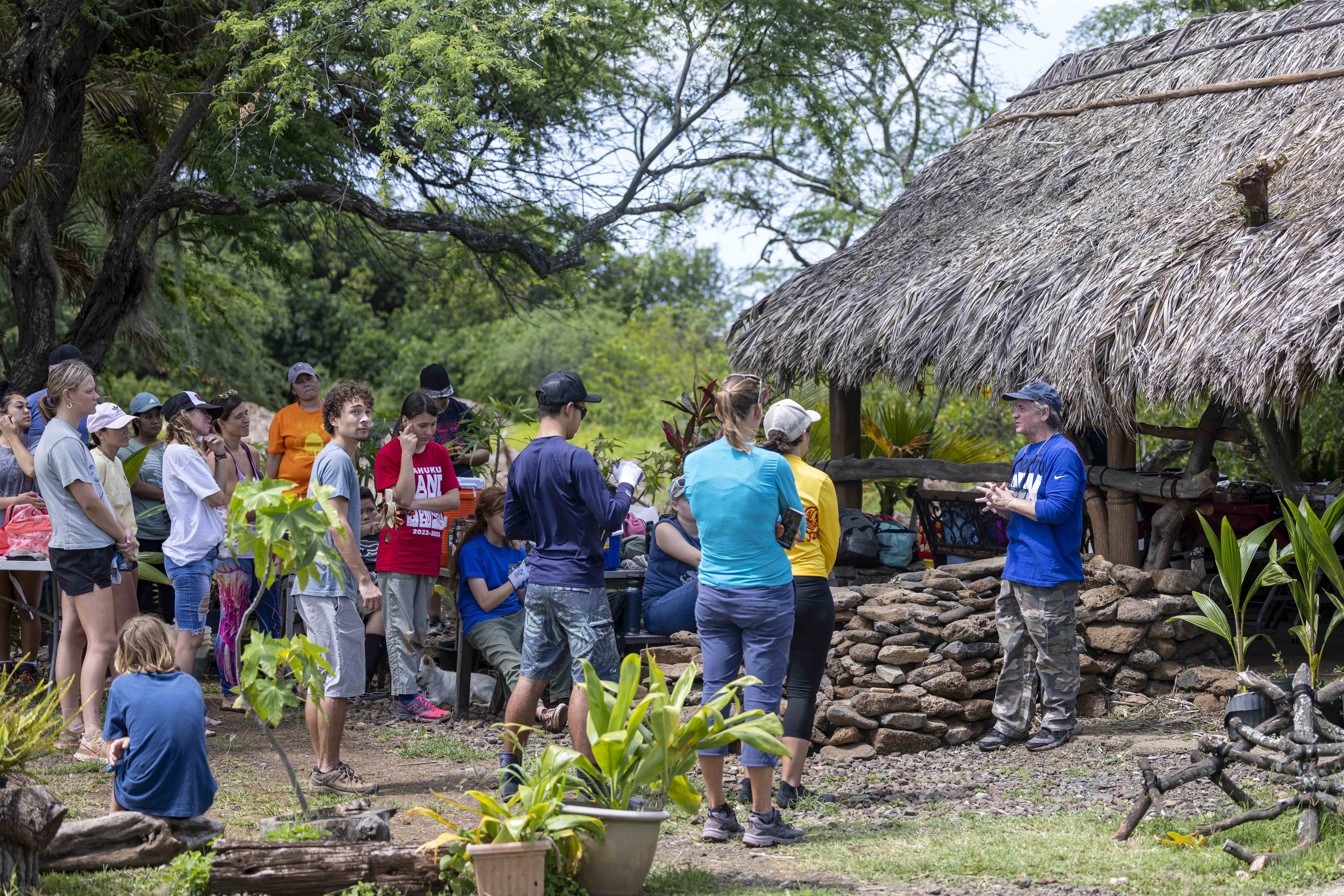 A group of people stand near a thatched-roof hut