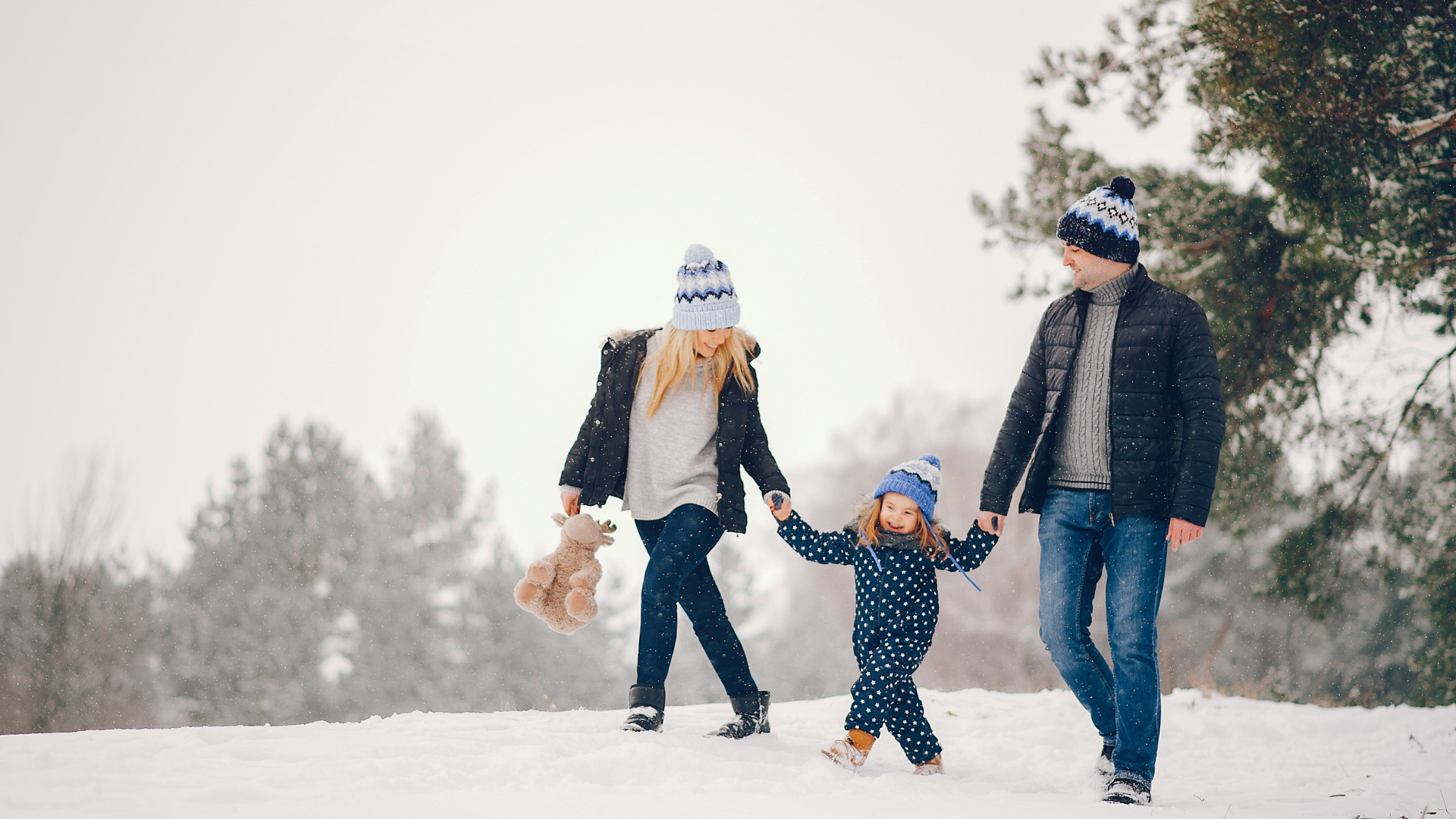 A couple walks with their young child in the snow.