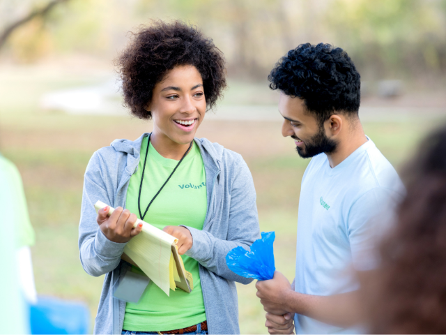 A woman points out something on a clipboard to a man wearing a shirt that says "volunteer"