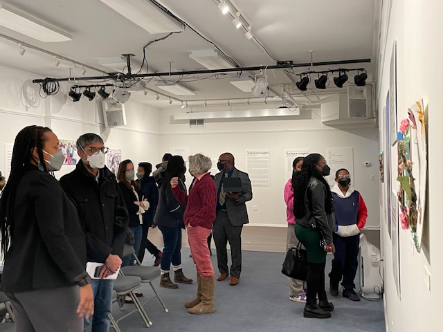 A group of people stand in an art gallery with white walls and spotlights