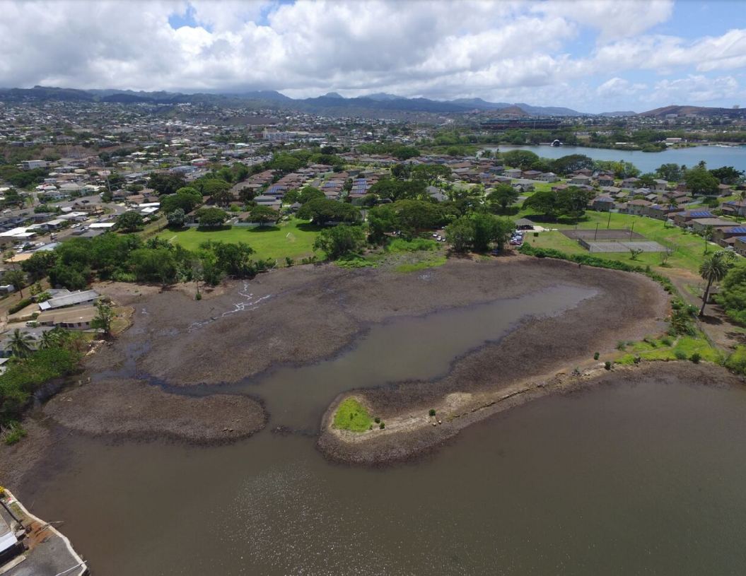 Aerial photo of a muddy, desolate-looking pond located near Navy barracks. The mountains of O'ahu are in the distance.