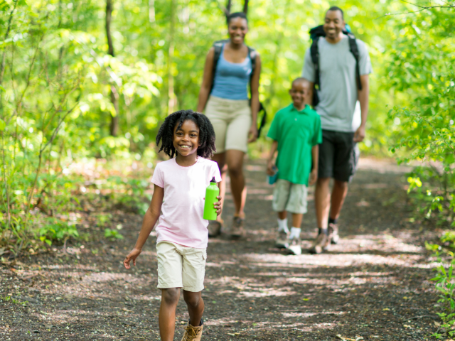 A young girl walks ahead of her family on a hiking path through a forest