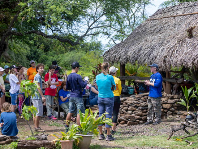 A group of people stand near a thatched-roof hut