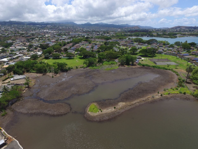 Aerial photo of a muddy, desolate-looking pond located near Navy barracks. The mountains of O'ahu are in the distance.