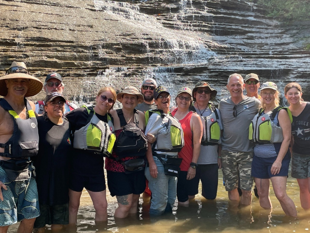 A group of people wearing lifejackets stand in front of a waterfall