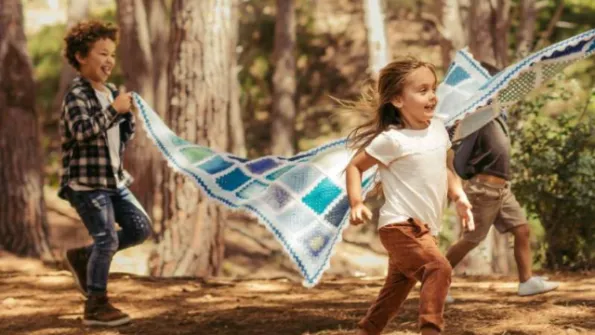 Two children holding a blanket up and running through the forest