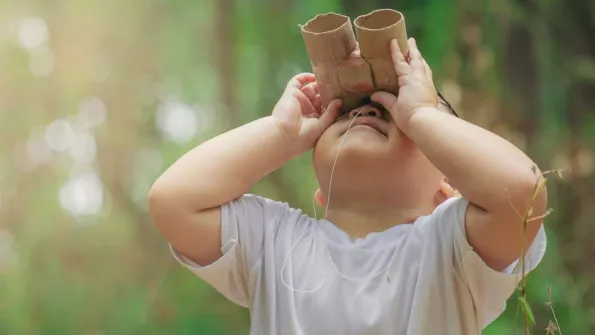Young child outdoors with paper bionoculars looking up 