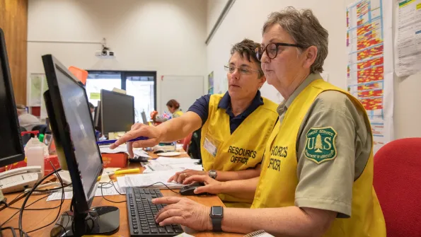 Two women wearing US Forest Service uniforms work together at a desk