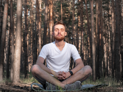 A man sits cross-legged on the ground surrounded by forest