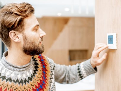 Man in sweater adjusting thermostat