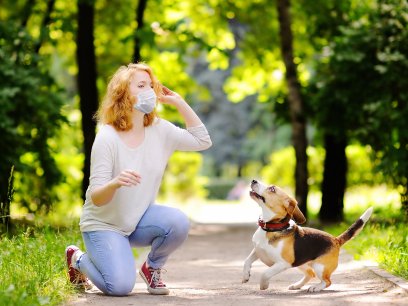 Woman in a face mask at the park with her dog