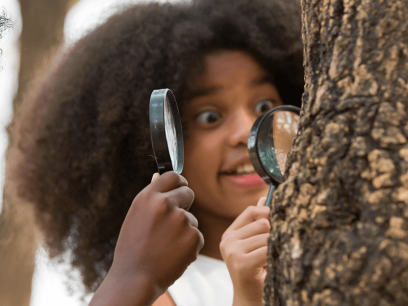 two children holding magnifying glasses and looking at a tree