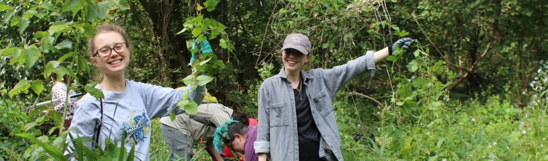 Two National Public Lands Day volunteers hold up invasive species of plant they collected in the forest