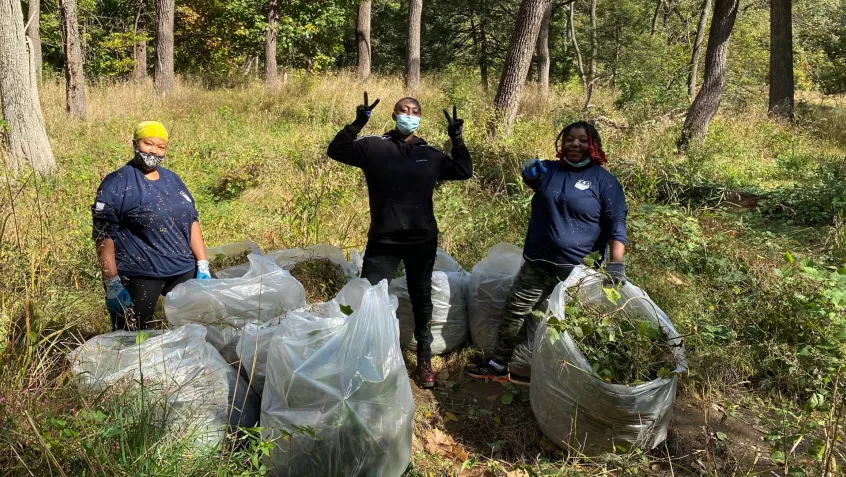three women stand with large plastic bags full of invasive weeds collected during National Public Lands Day volunteering
