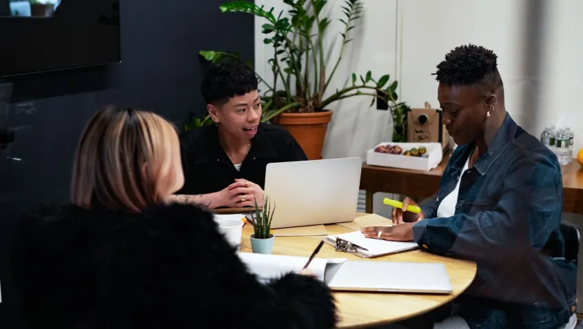 Three people sitting around a desk having a meeting