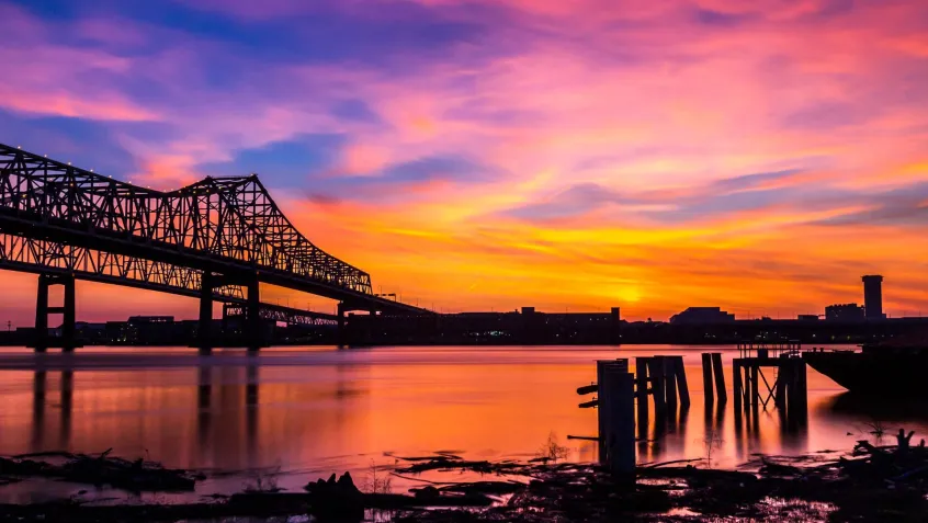 A view of a bridge over the Mississippi River in New Orleans at sunset.