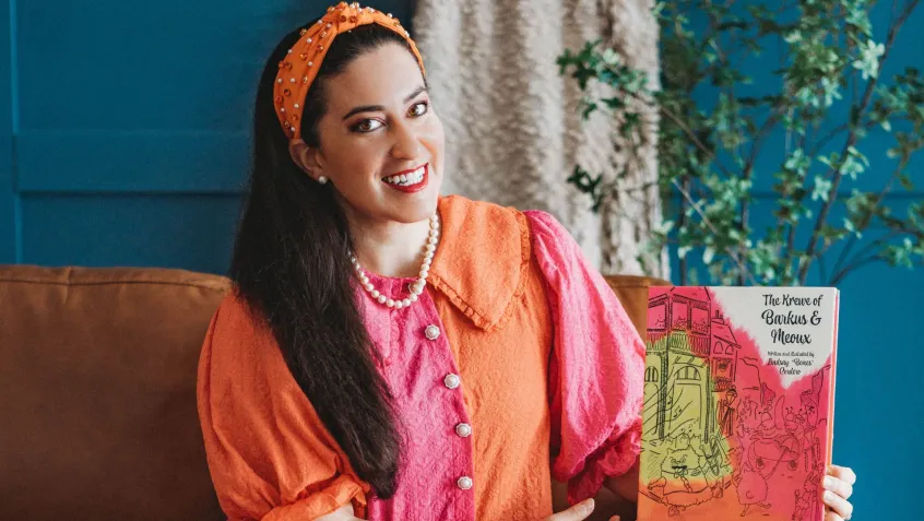 Artist Lindsay Cordero sits holding her picture book The Krewe of Barkus and Meoux