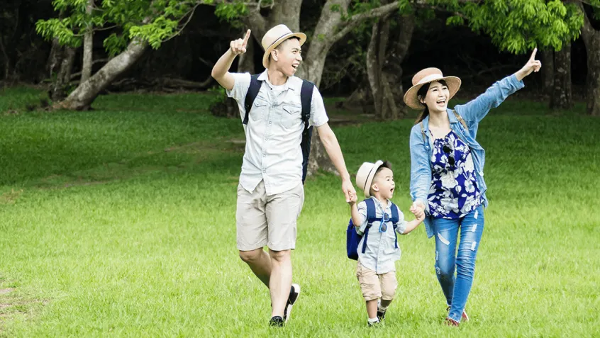 Family with young son walking and pointing to things on a trail in a green field near