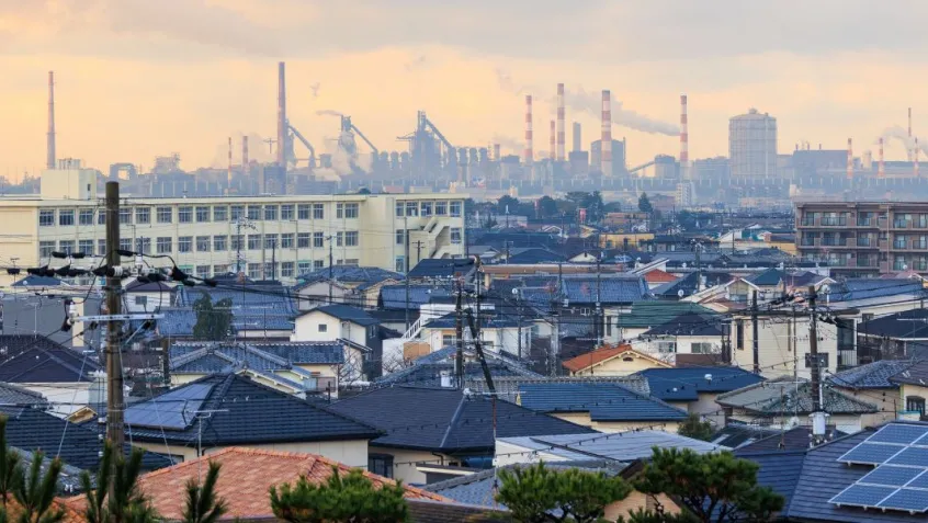 view of rooftops and homes with an industrial center and smokestacks in the distance