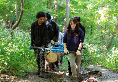 a group of young volunteers carries a large log on a trail during National Public Lands Day