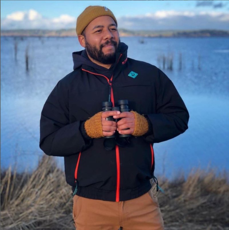 a man stands near a wetland with smiling with a pair of binoculars