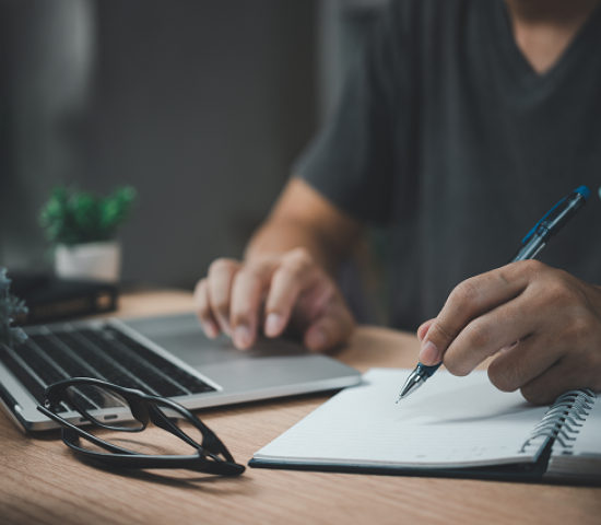 Person typing on computer while writing on a notepad