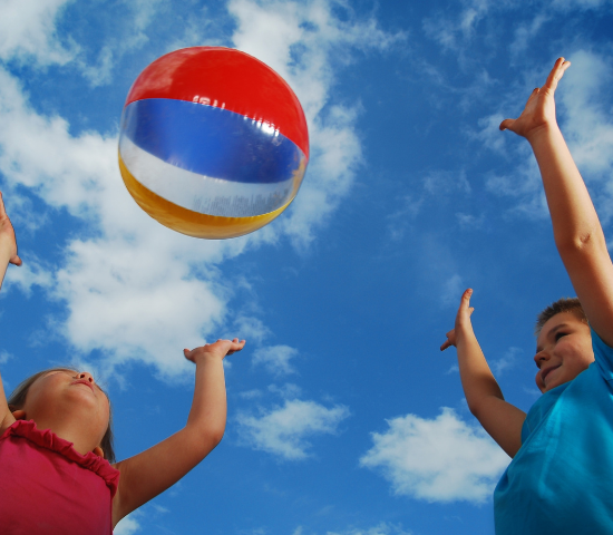 Two children tossing a beachball towards the sky