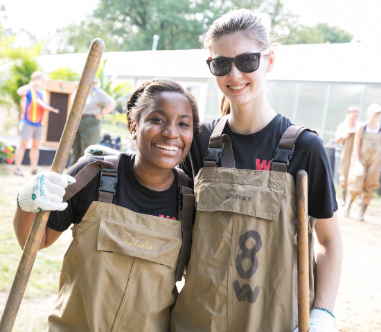 Two girls in bibs and digging equipment outdoors