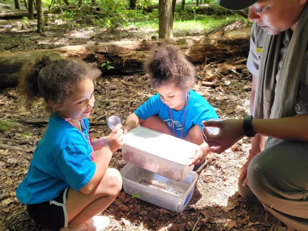 a park ranger helps two young students during an outdoor education lesson