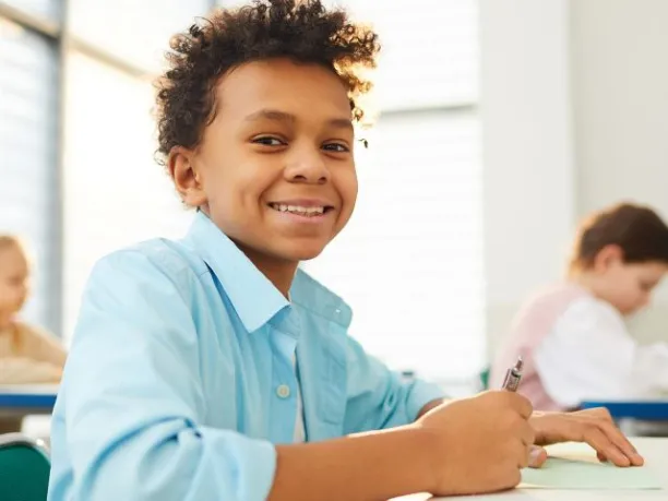 a middle school student smiles while sitting at a desk