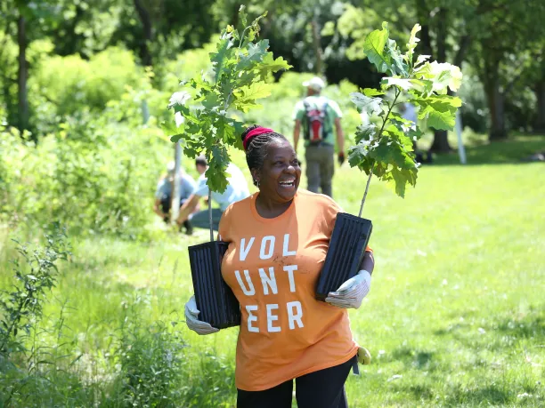 woman holding tree saplings and smiling while volunteering outdoors