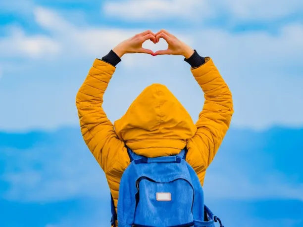 person standing in front of distant mountain range making heart shape with hands