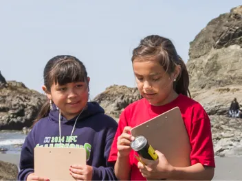 Two young girls outdoors looking at water samples and taking notes