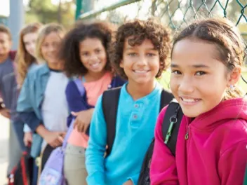 a diverse group of young students stands in a line along a fence all smiling