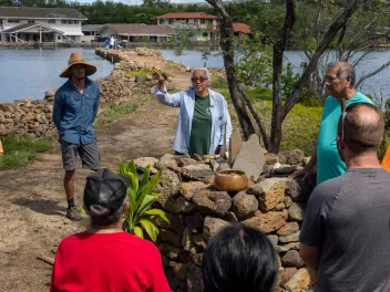 A group gathers around a stone altar as an elder from the Native Hawaiian community explains the significance of the sacrificial offerings placed there