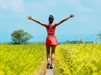 A woman walking in a green field with her arms open wide.