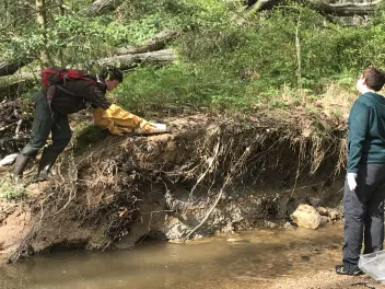 Two people pick up garbage from a stream